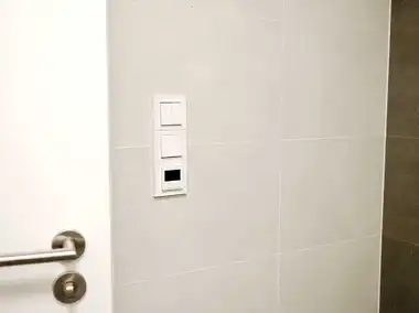 B&iacute;l&yacute; digit&aacute;ln&iacute; termostat Levit v koupelně ve trojr&aacute;mečku s vyp&iacute;nači